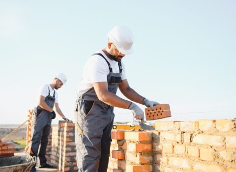 A team of Indian construction workers in overalls and hard hats are building a brick wall.