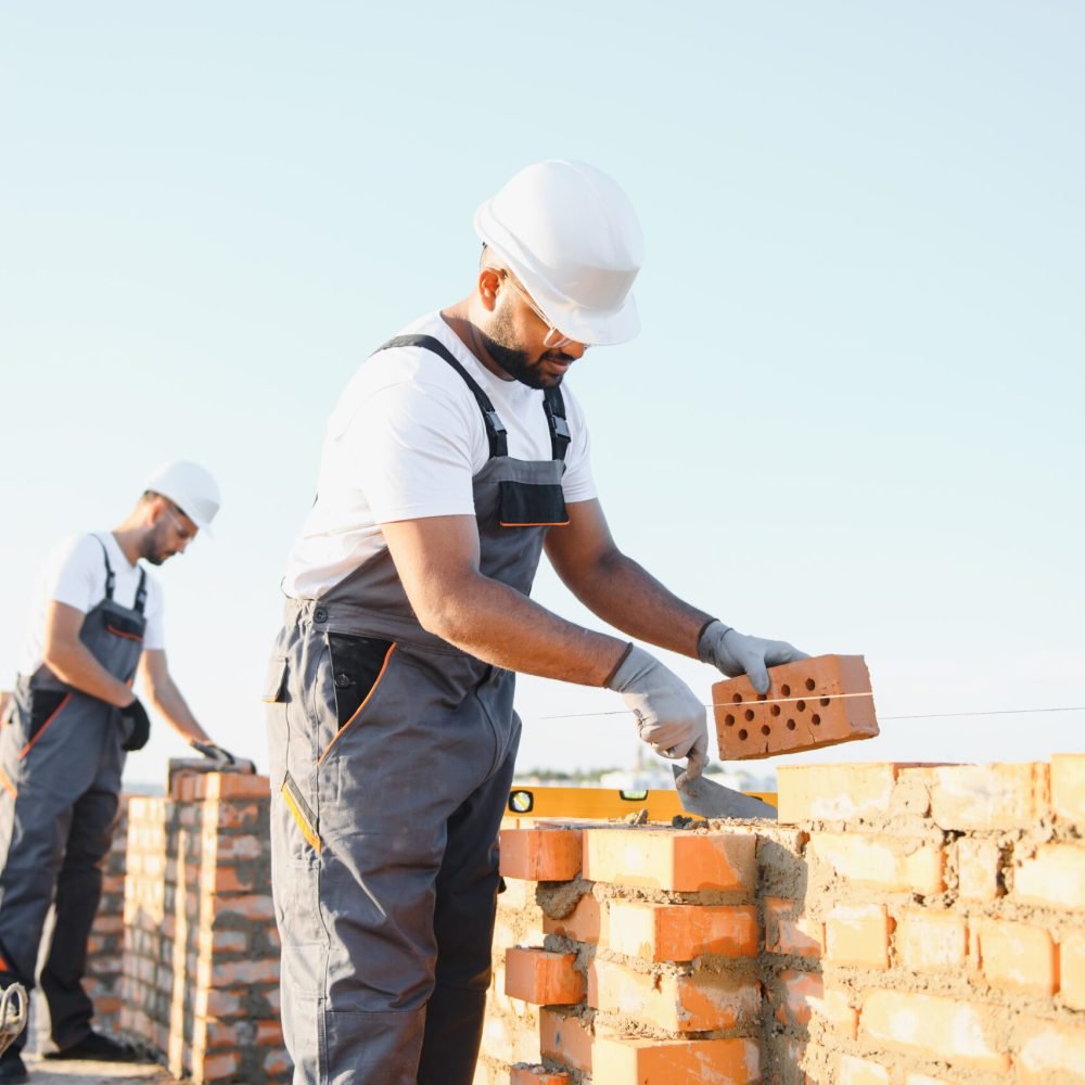 A team of Indian construction workers in overalls and hard hats are building a brick wall.